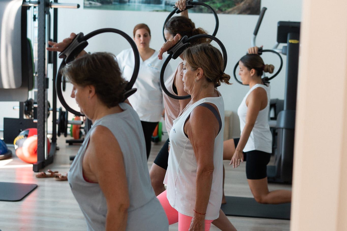 Alumnas de pilates en zancada sostienen el aro por encima de la cabeza.